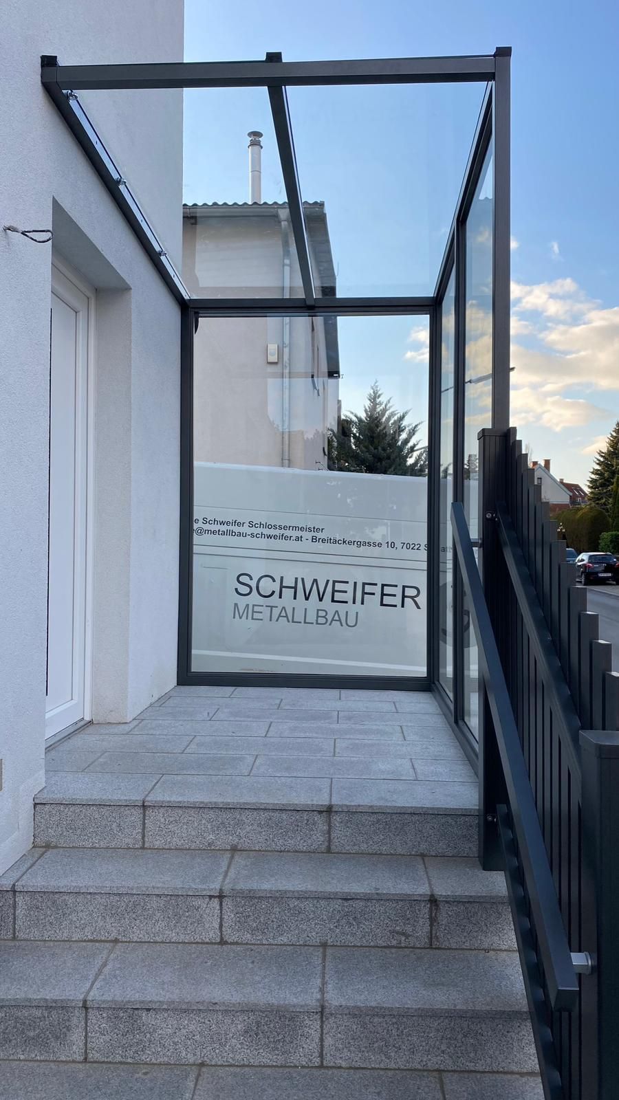 Ein weißes Gebäude mit einer Treppe nach oben und einer Glaswand, dahinter steht ein Firmenwagen mit der Aufschrift ,,Schweifer Metallbau