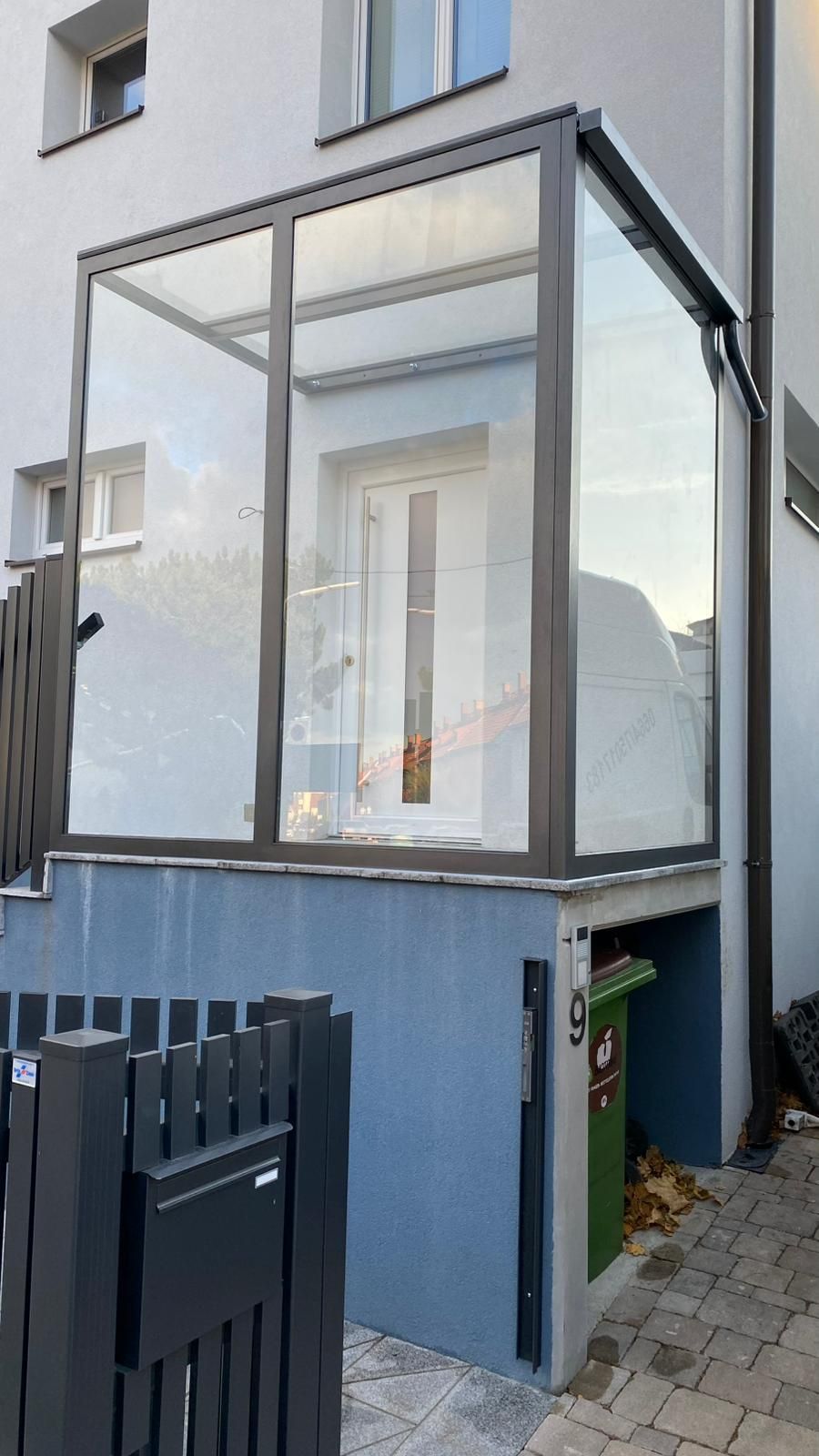 Ein Haus mit einer Glasveranda und einem Zaun davor.