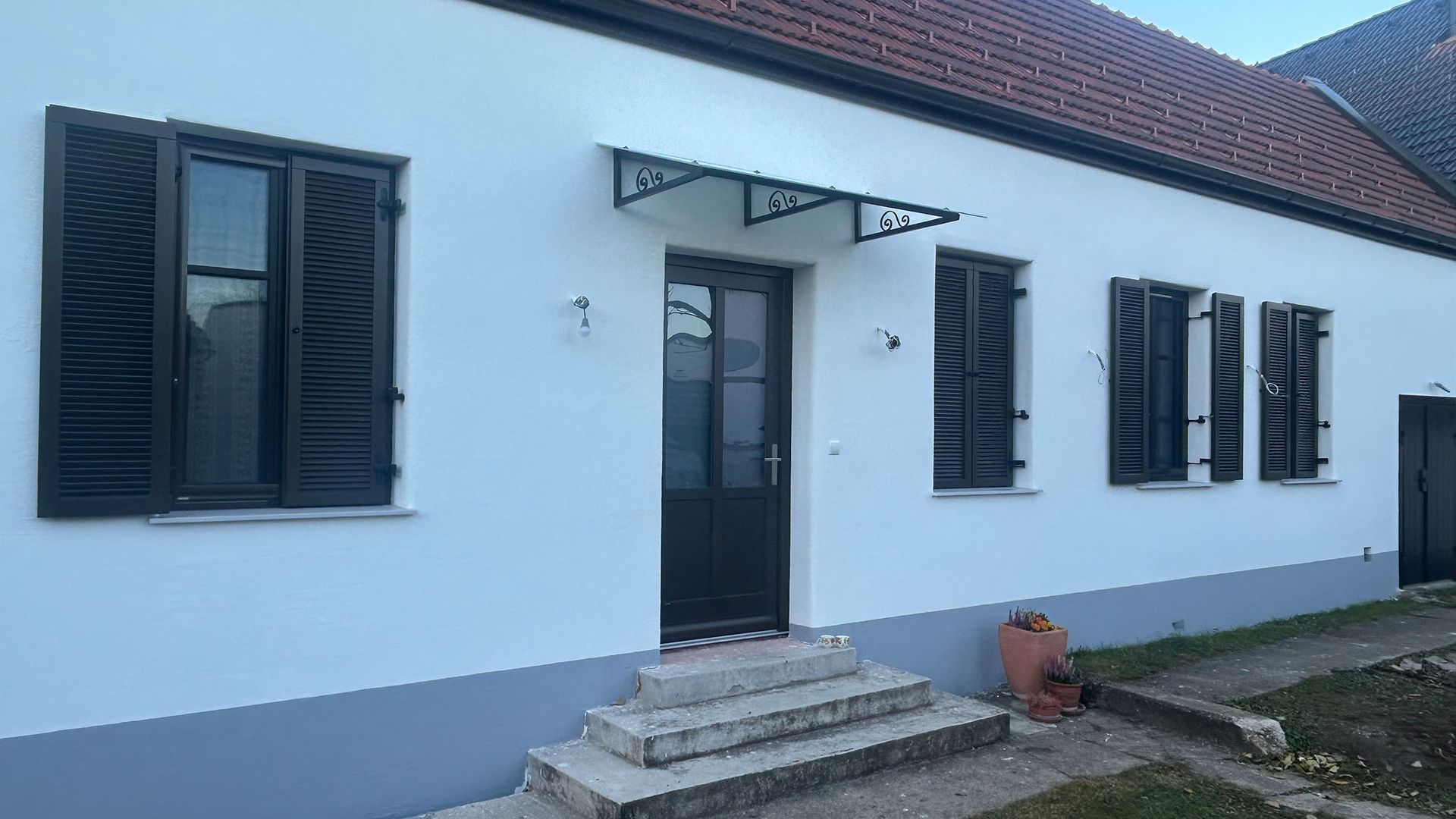 Ein weißes Haus mit schwarzen Fensterläden, Türen und einer Glasüberdachung bei der Tür.