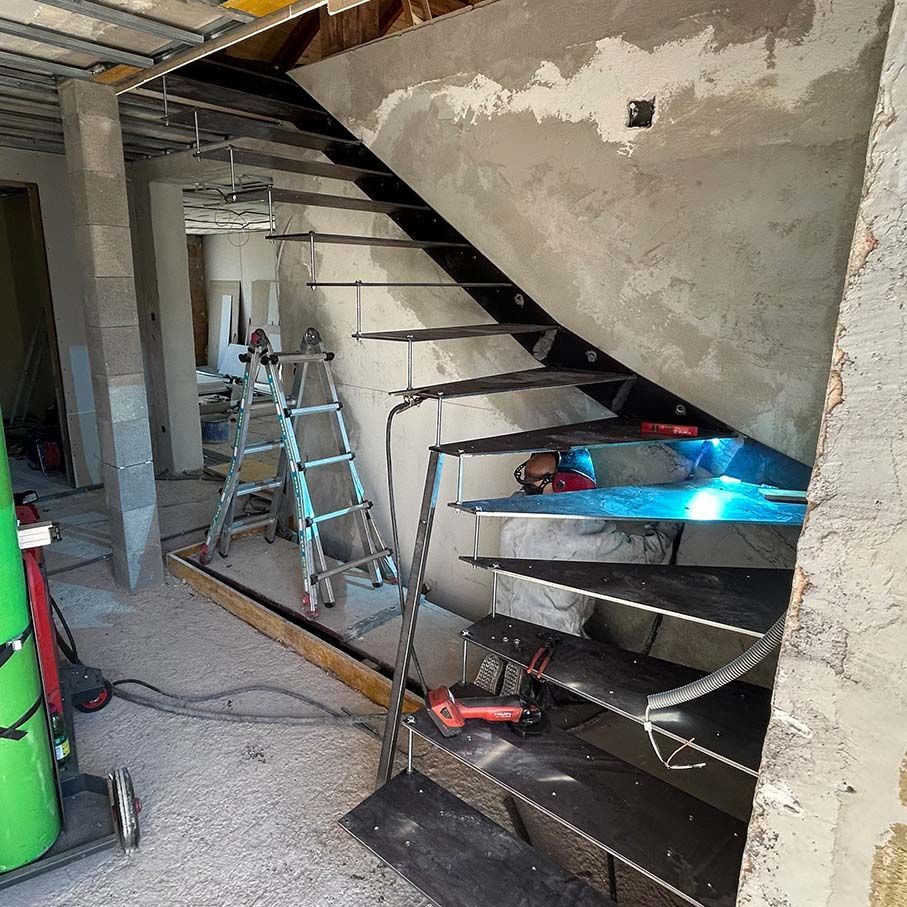 Baustelle mit einer teilweise errichteten Stahltreppe und freiliegenden Betonwänden. Werkzeuge sind vorhanden.
