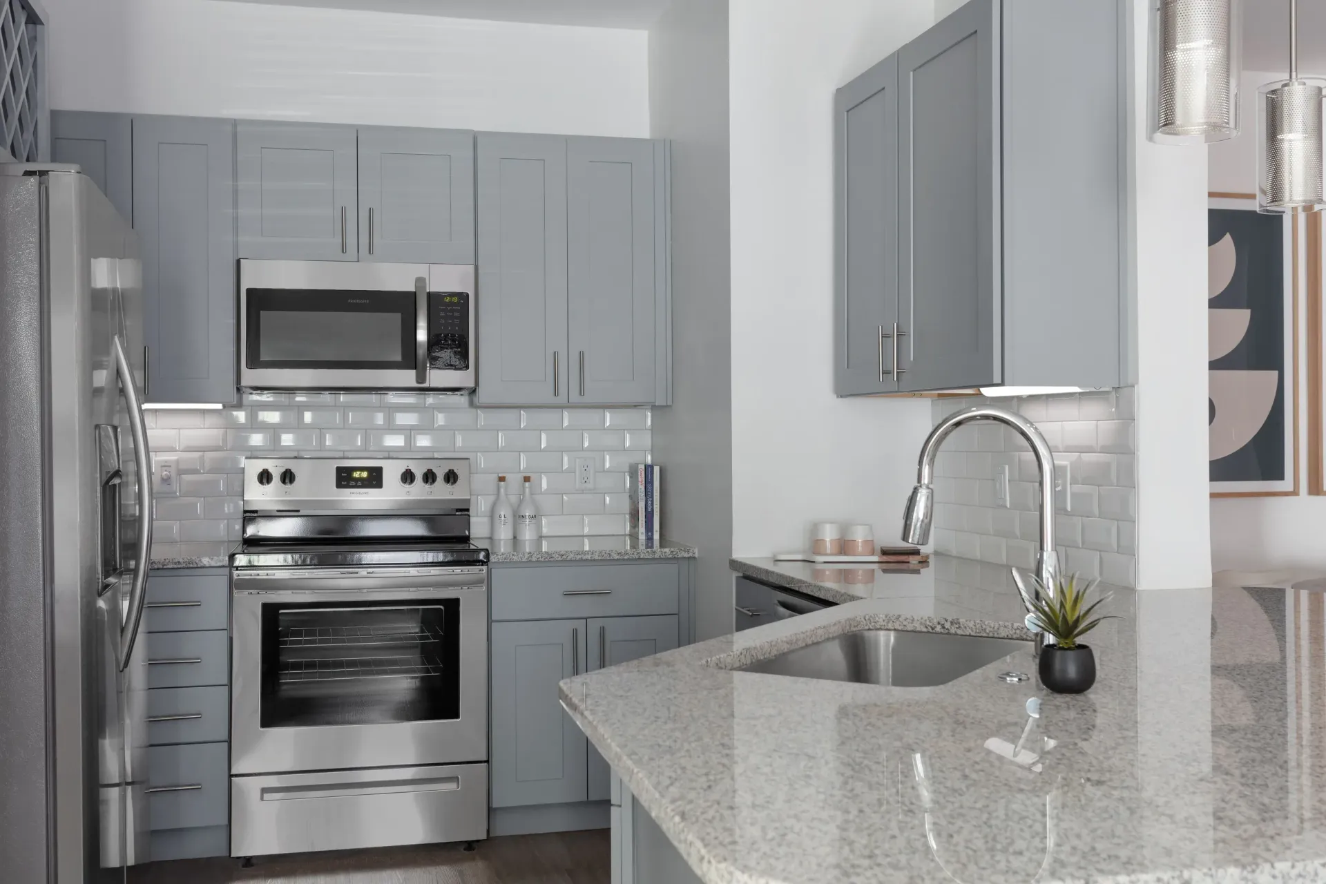 Modern grey kitchen with stainless steel appliances, granite island, and white subway tile backsplash.