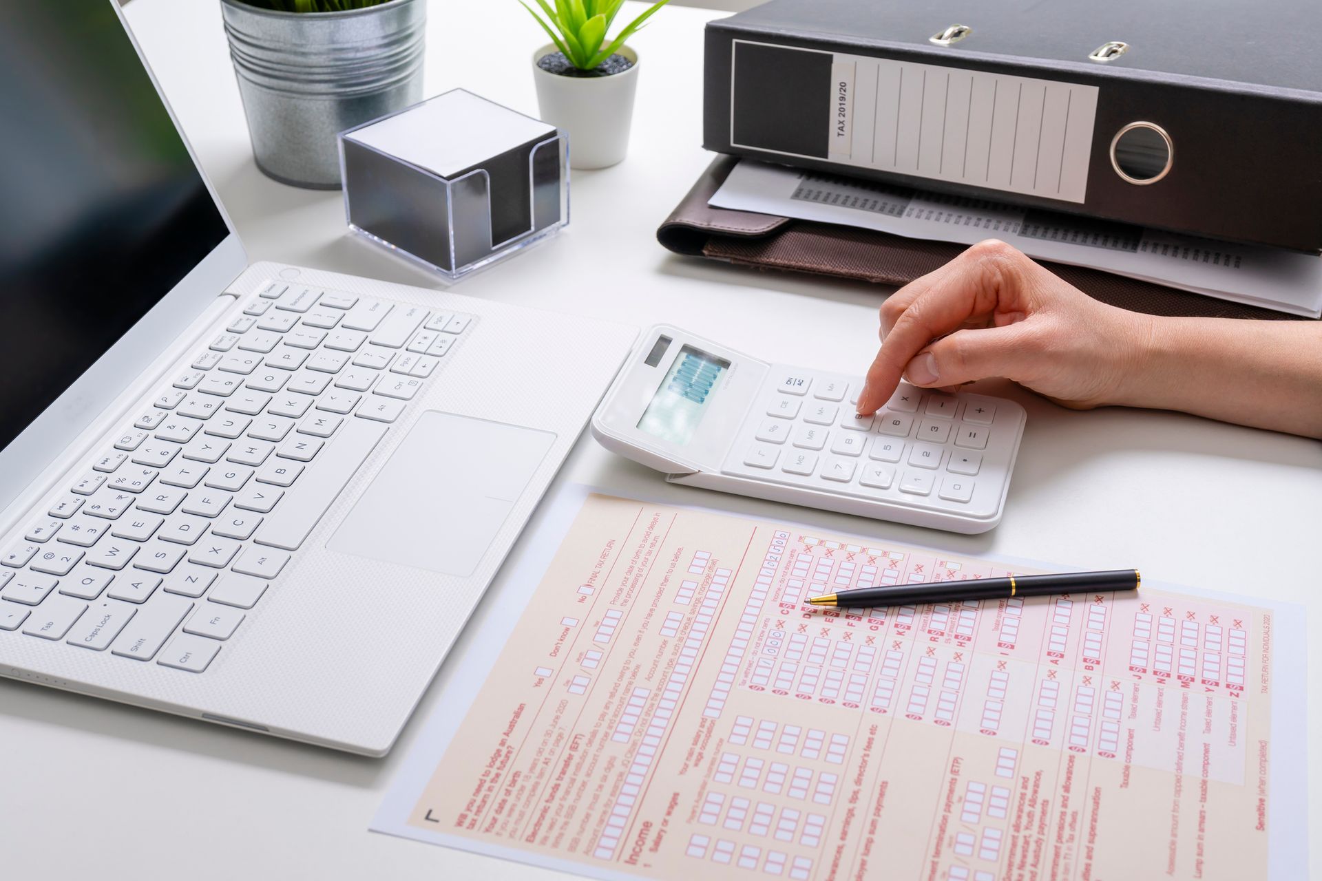 A person is using a calculator on a desk next to a laptop.
