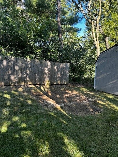 A shed is sitting in the middle of a lush green yard next to a wooden fence.