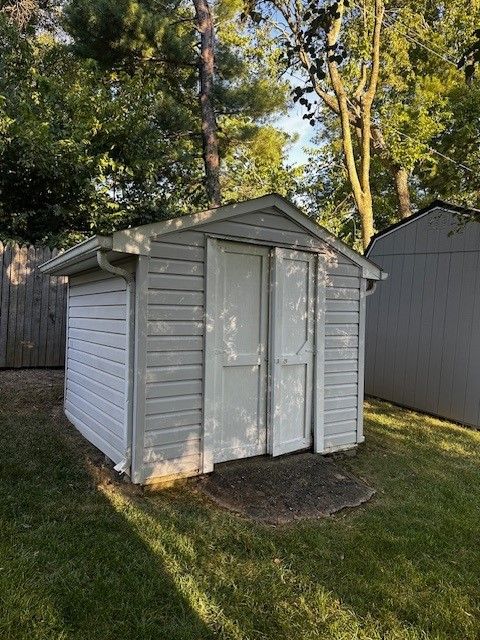 A small white shed is sitting in the middle of a lush green yard.