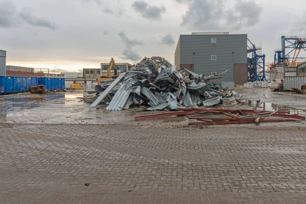 Pile of metal debris at industrial demolition site with containers and machinery.