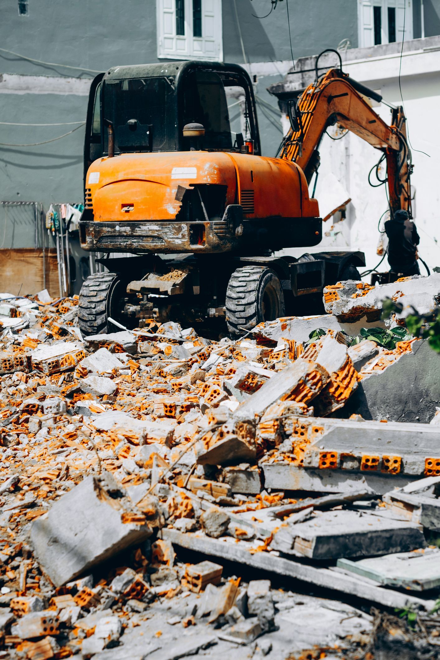 Orange excavator clearing debris after structural teardown by demolition services team.