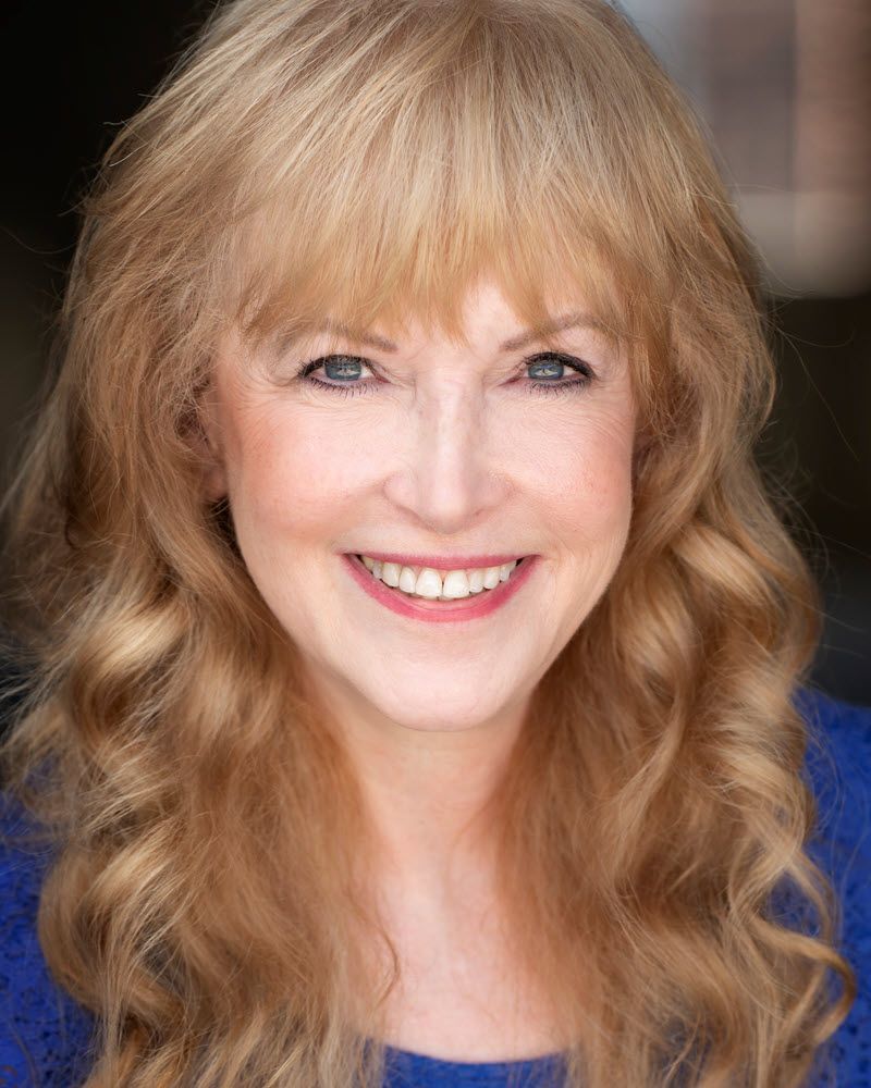 Blond woman with bangs smiles, blue shirt.