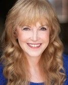 Blond woman with bangs smiles, blue shirt.