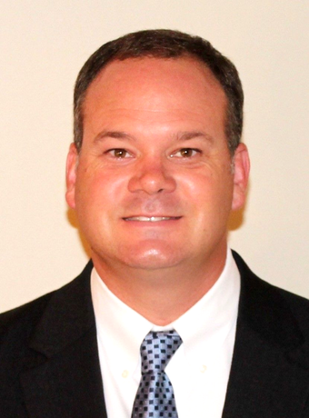 A man in a grey shirt is smiling for the camera