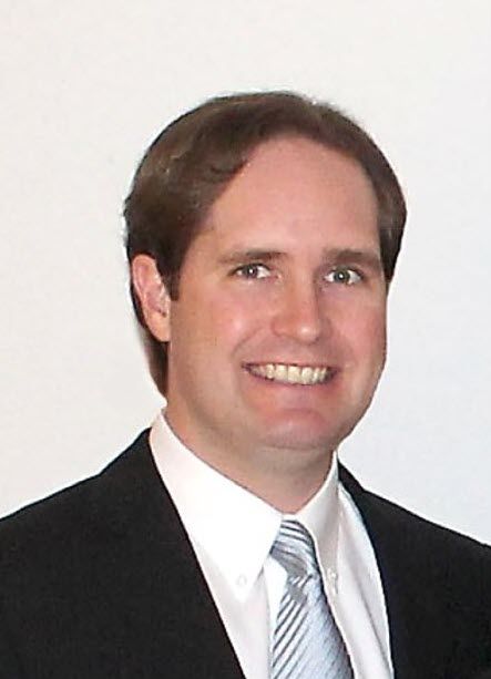 A man in a grey shirt is smiling for the camera