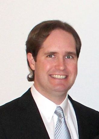 A man in a grey shirt is smiling for the camera