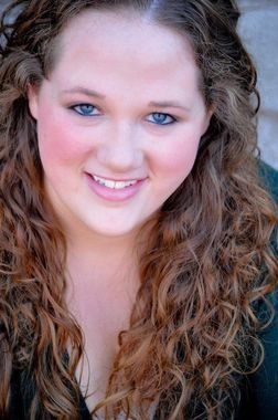 Woman with curly brown hair smiles; rosy cheeks, blue eyes, close-up shot.
