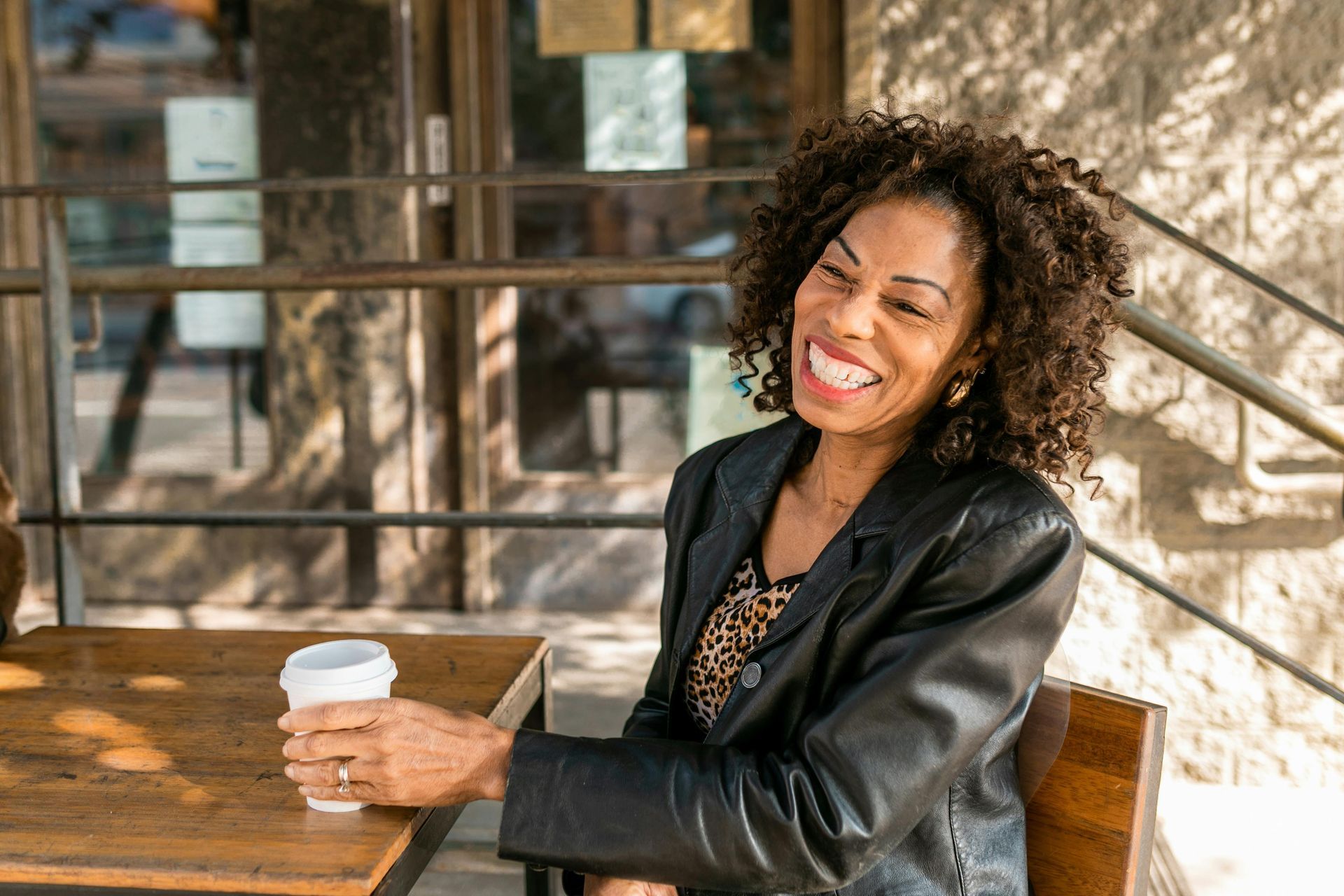 A woman is sitting at a table holding a pen and notebook and looking out the window.