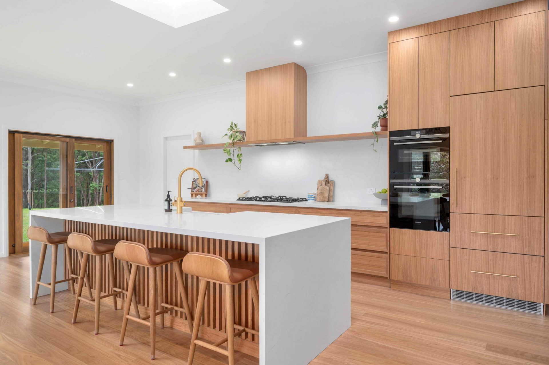 A Kitchen With Wooden Cabinets and Stools and a Large Island — Plumbe Joinery in Coffs Harbour, NSW