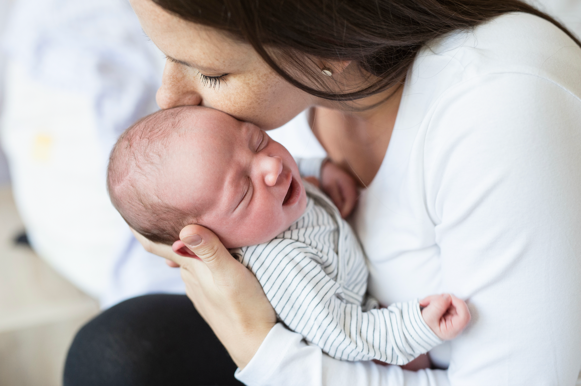 A woman is kissing a crying baby on the forehead.