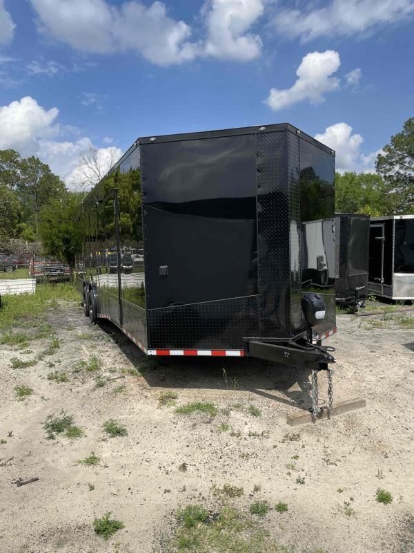 Black enclosed trailer parked on dirt, under a blue sky.