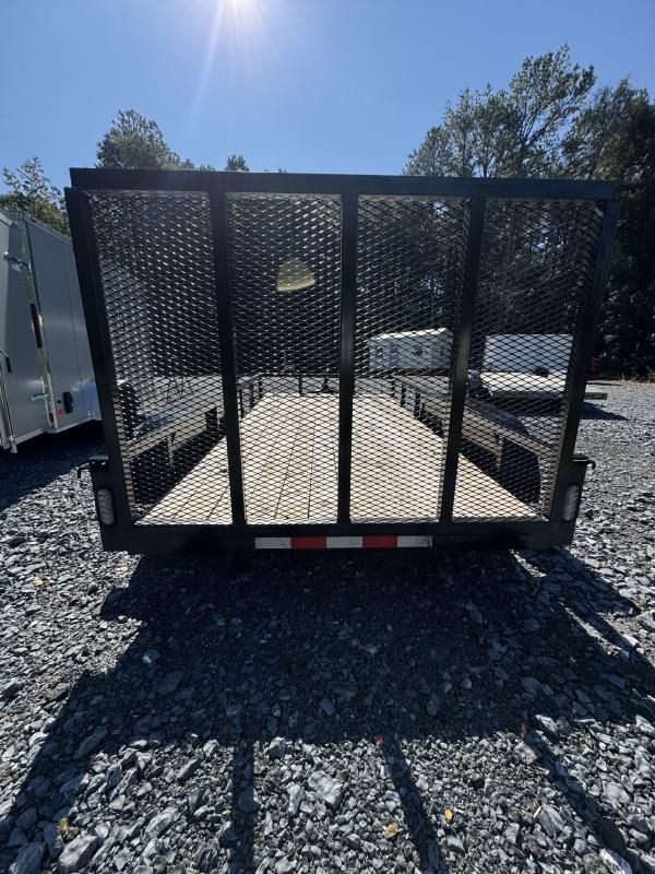 Black utility trailer with mesh sides and wooden deck on a gravel lot.