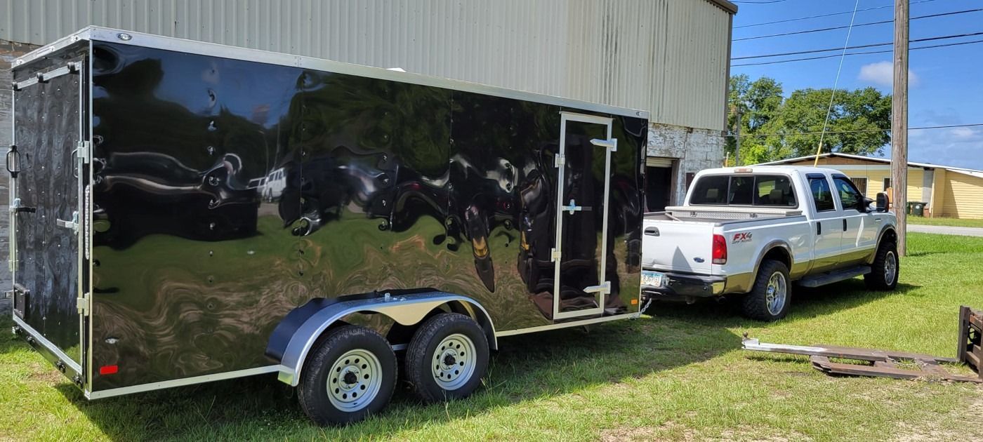 A white pickup truck towing a black enclosed trailer on a grassy lawn.