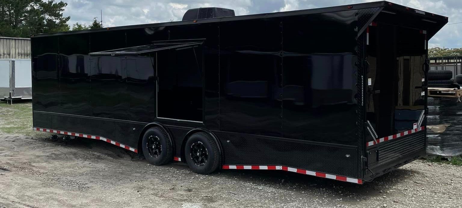 Black enclosed trailer with red and white trim on a gravel lot.