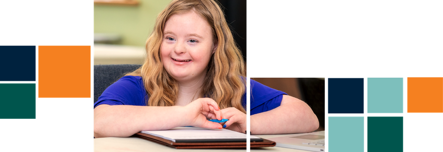 A young girl with down syndrome is sitting at a table writing in a notebook.
