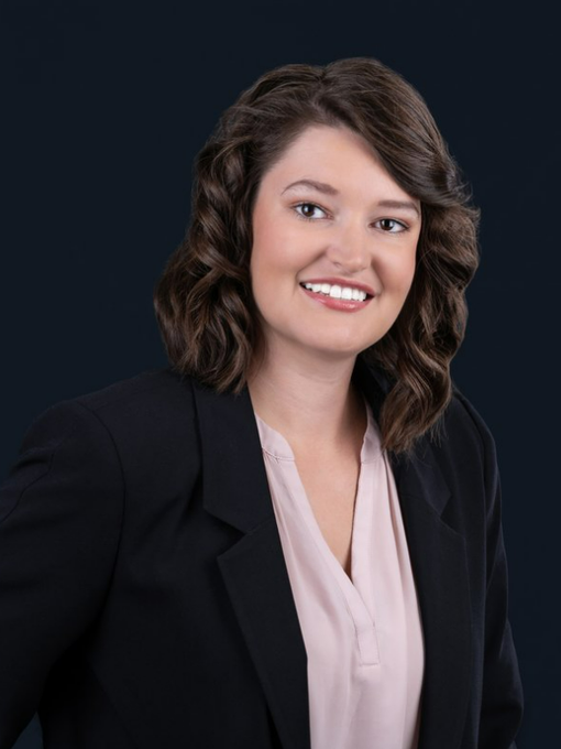 A woman wearing a black jacket and a pink shirt is smiling for the camera.