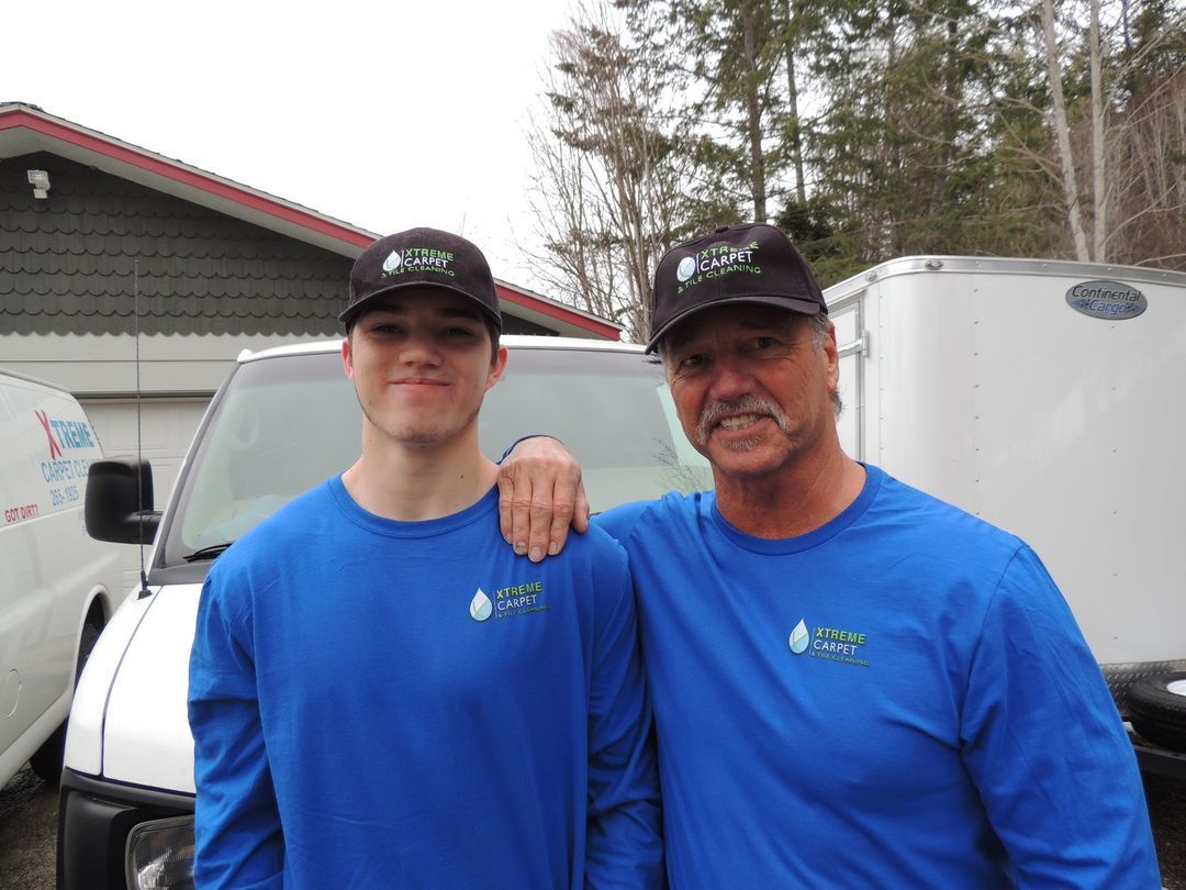 Two men in blue shirts are posing for a picture in front of a white van.