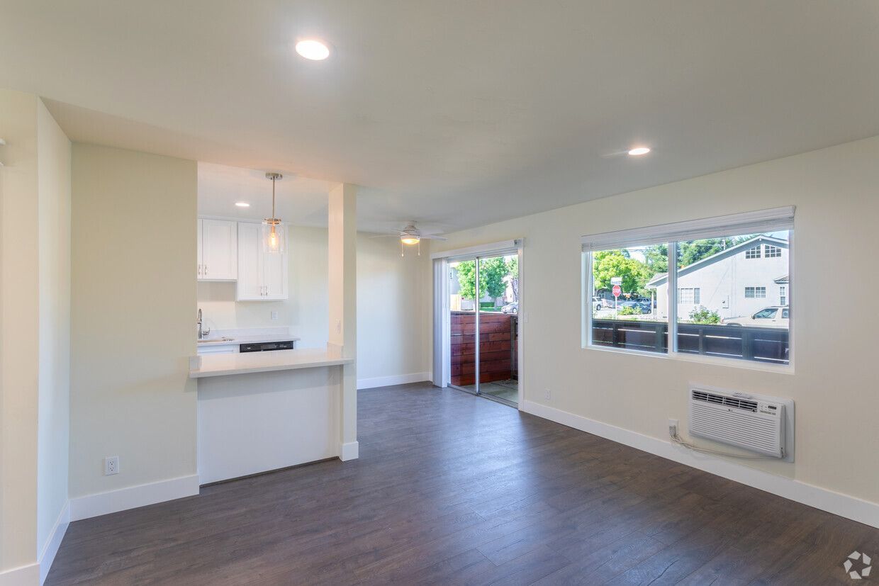 An empty living room with hardwood floors and sliding glass doors leading to a kitchen.