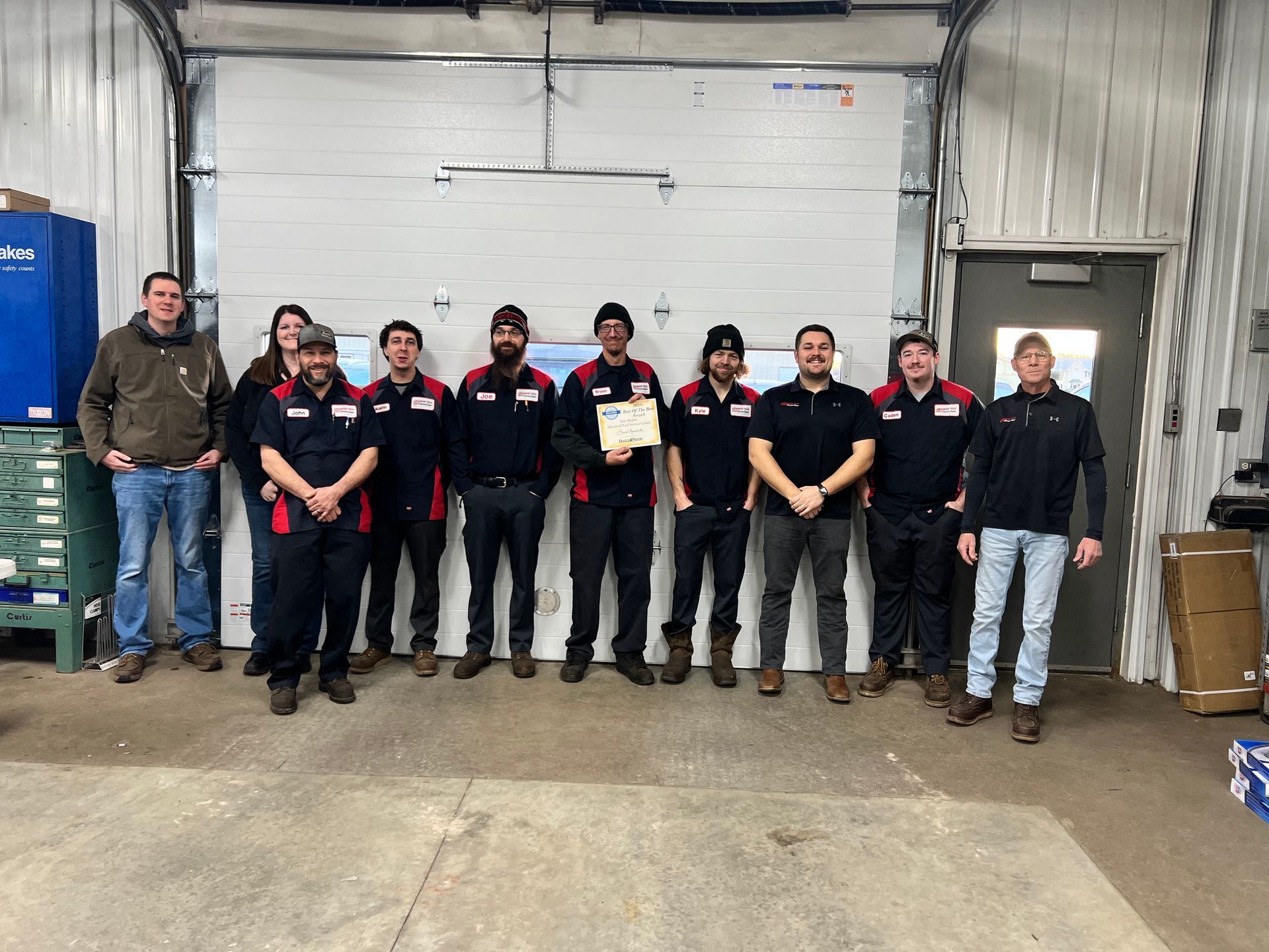 Two mechanics smiling while working on a car in a shop. One holds a tablet.