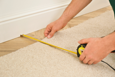 In this image, we see a skilled flooring San Jose Flooring Pros installer meticulously fitting a beige textured carpet flooring san jose ca against a wall with precision. The installer's hands are shown using a specialized tool to tuck the edge of the carpet neatly beneath the white baseboard, ensuring a clean and smooth finish along the perimeter of the room floor installation san jose. The attention to detail highlights the quality workmanship and expertise offered by the San Jose flooring Pros. The installer's carpet installation san jose focus and expertise are evident in the careful placement of the carpet, showcasing their dedication to providing a flawless final result for the client. This image captures the professionalism and precision that goes into the meticulous installation of san jose flooring, demonstrating the commitment to excellence in every aspect of the job.