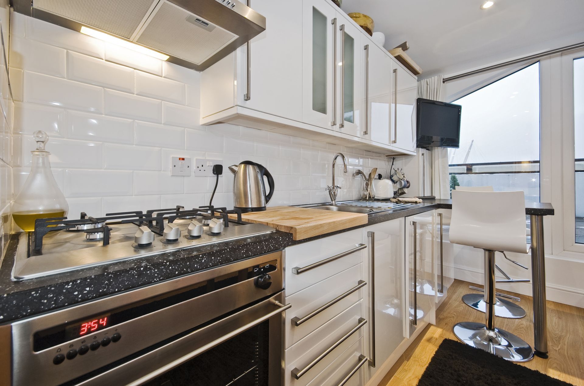 Compact modern kitchen with white cabinets, gas stove, kettle, and breakfast bar by a window