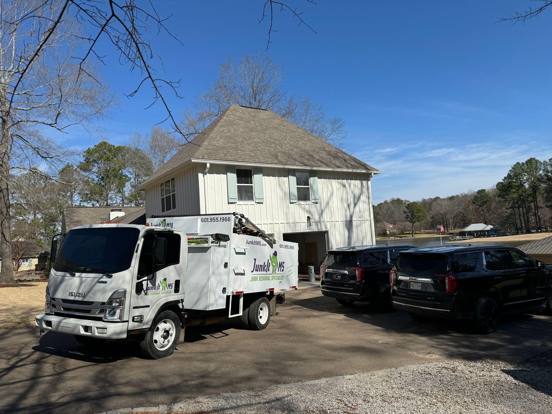 Tree service truck parked in front of a house with two black SUVs; bright, sunny day.