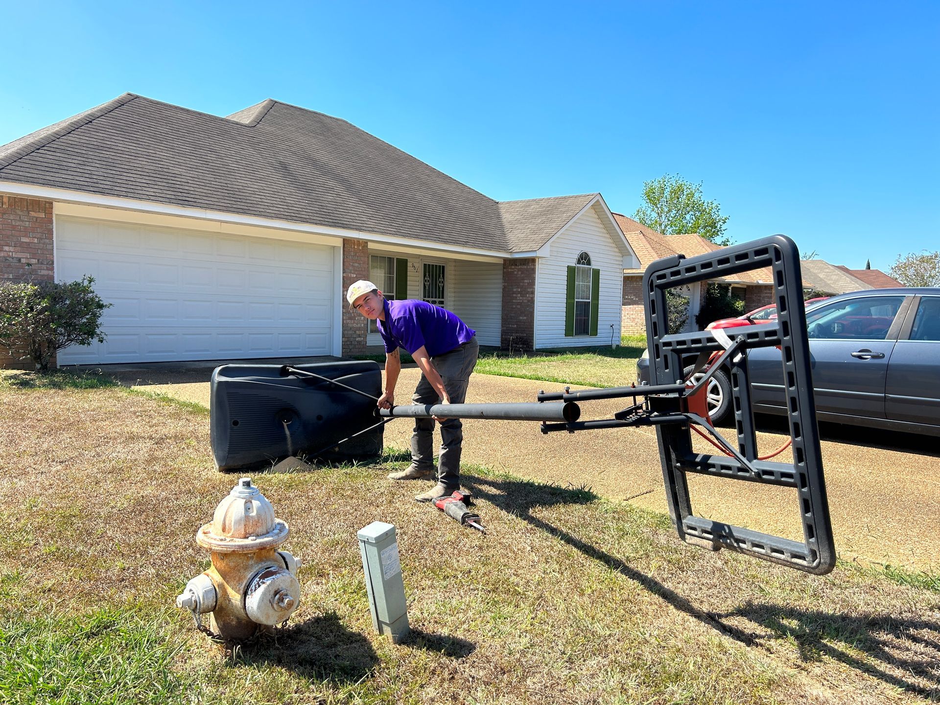 Man working with equipment near a house and a fire hydrant on a sunny day.