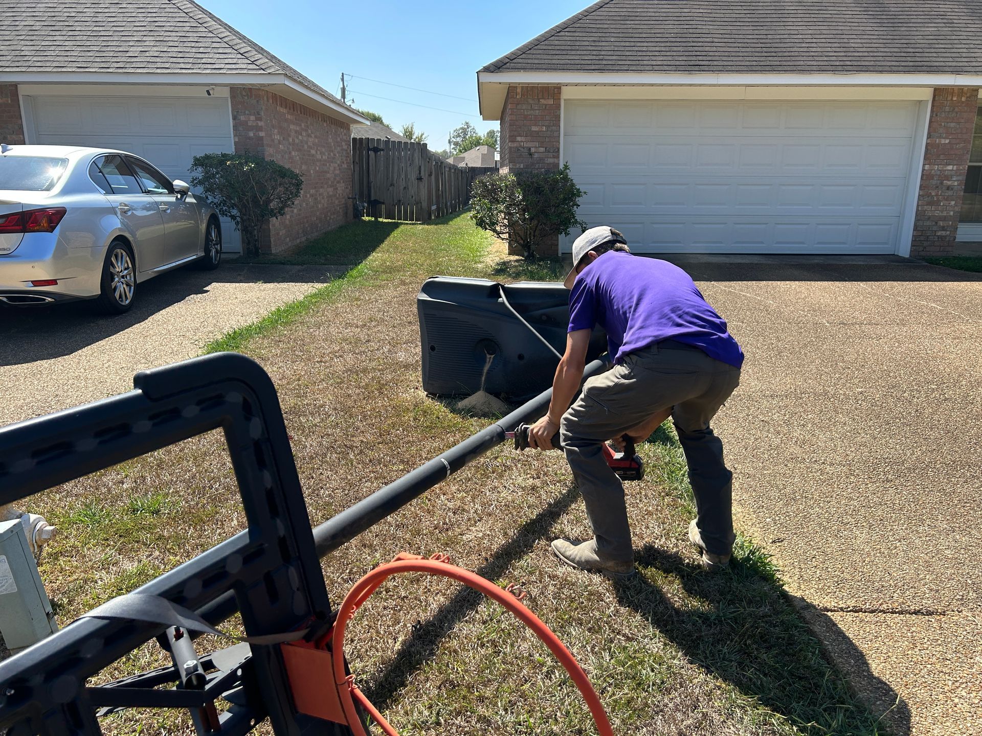 A person in a purple shirt is installing a basketball hoop in a driveway.