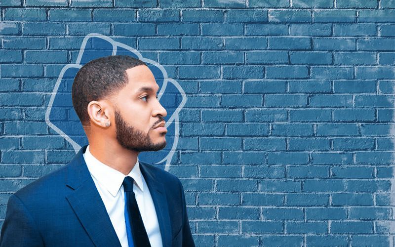 A man in a suit and tie is standing in front of a blue brick wall.