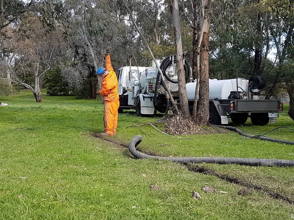 a man in an orange suit is standing next to a vacuum truck in a park .