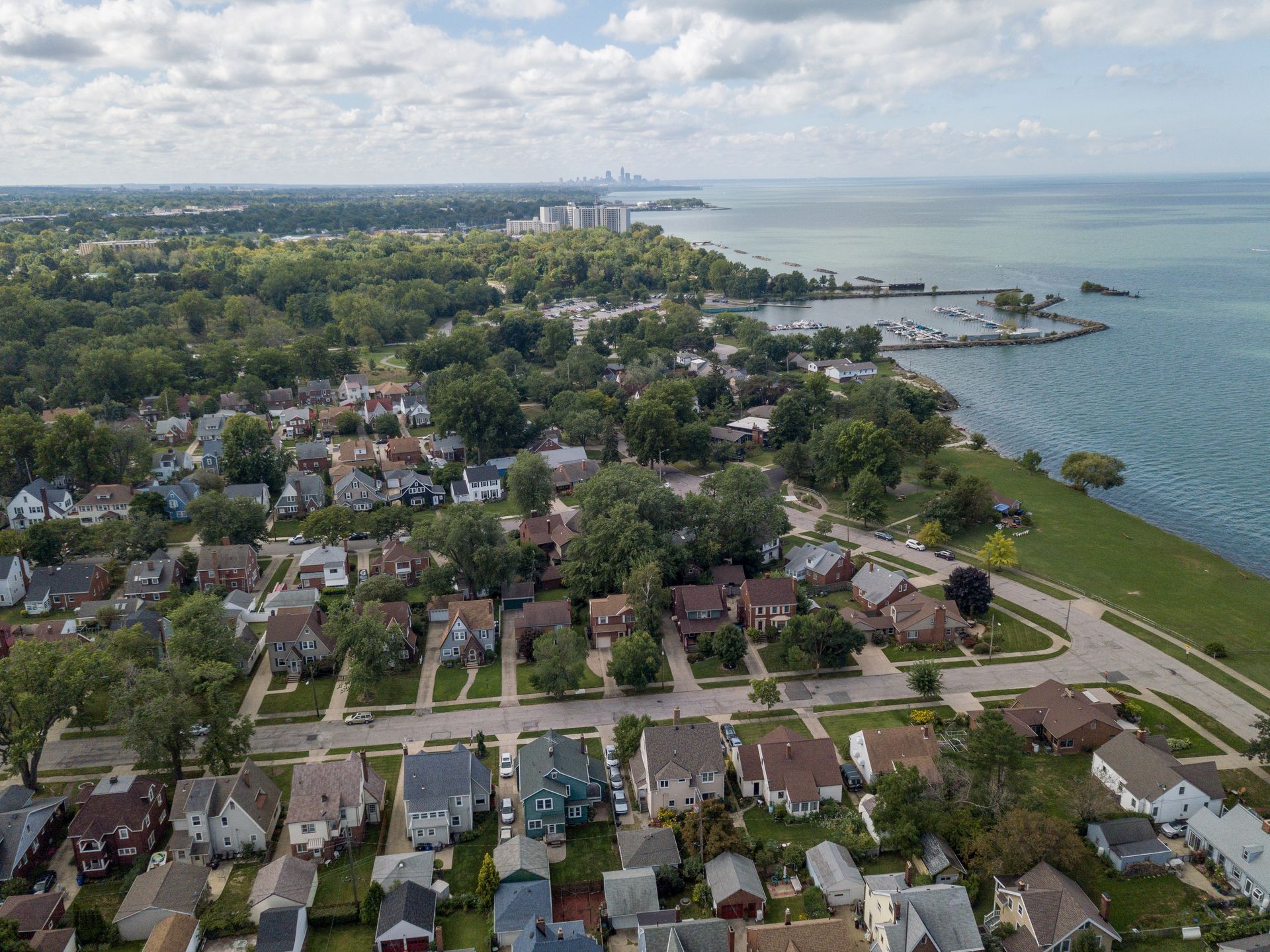 Aerial view of a residential neighborhood along a shoreline with a body of water on a partly cloudy day.