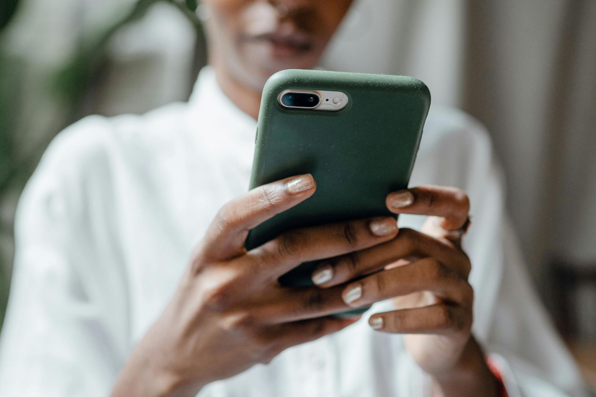 Person holding a green smartphone, focused on the screen, indoors.
