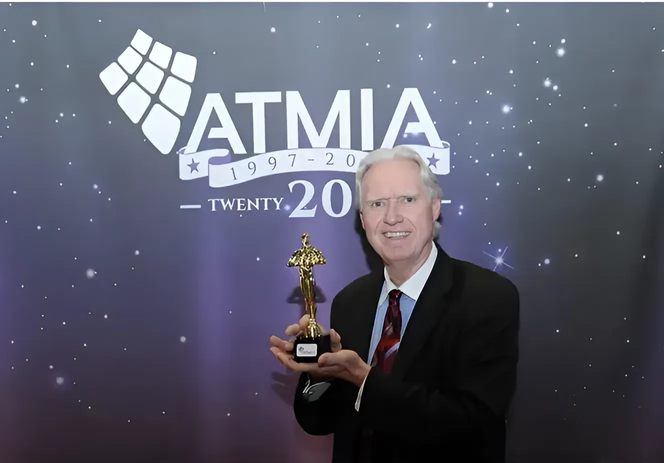 A man holding a trophy in front of a sign that says ATMIA.