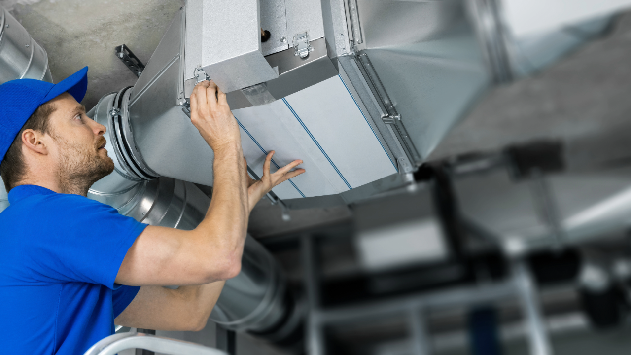 A man is working on a ventilation system in a building.