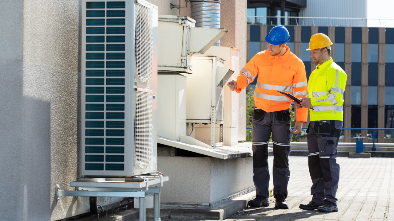 Two men are standing next to each other on a roof looking at a machine.