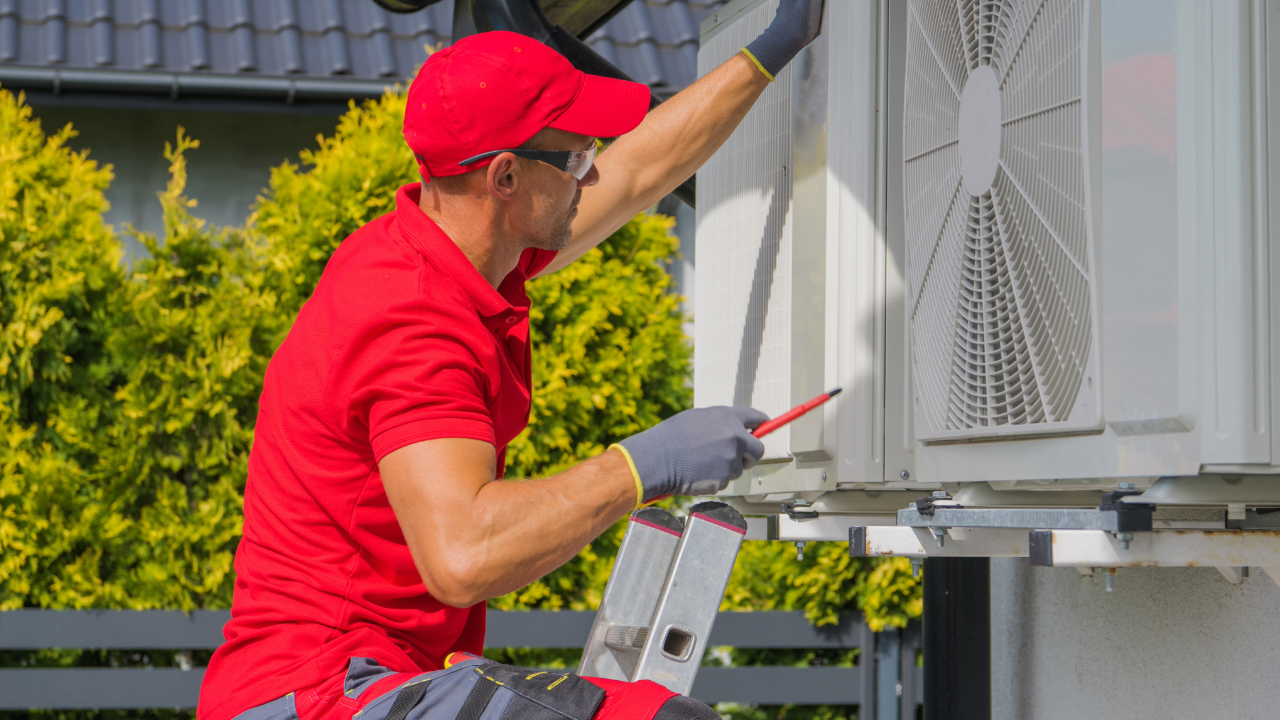 A man is standing on a ladder fixing an air conditioner.