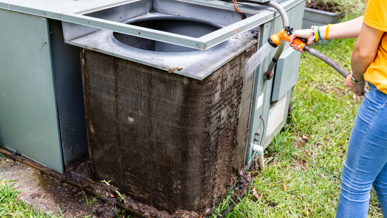 A woman is cleaning a dirty air conditioner with a hose.