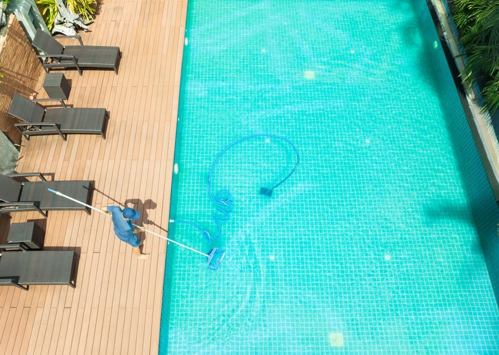 A man is cleaning a swimming pool with a vacuum cleaner.