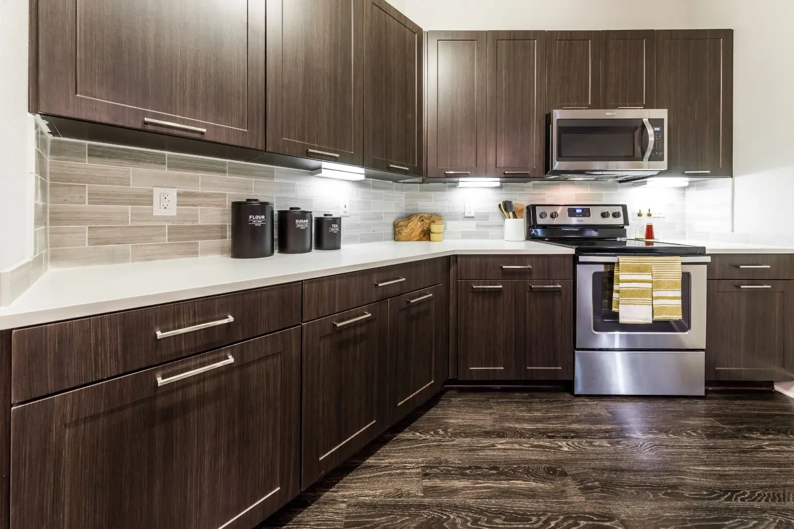 Modern kitchen with dark wood cabinets, white countertops, stainless steel appliances, and a subway tile backsplash.