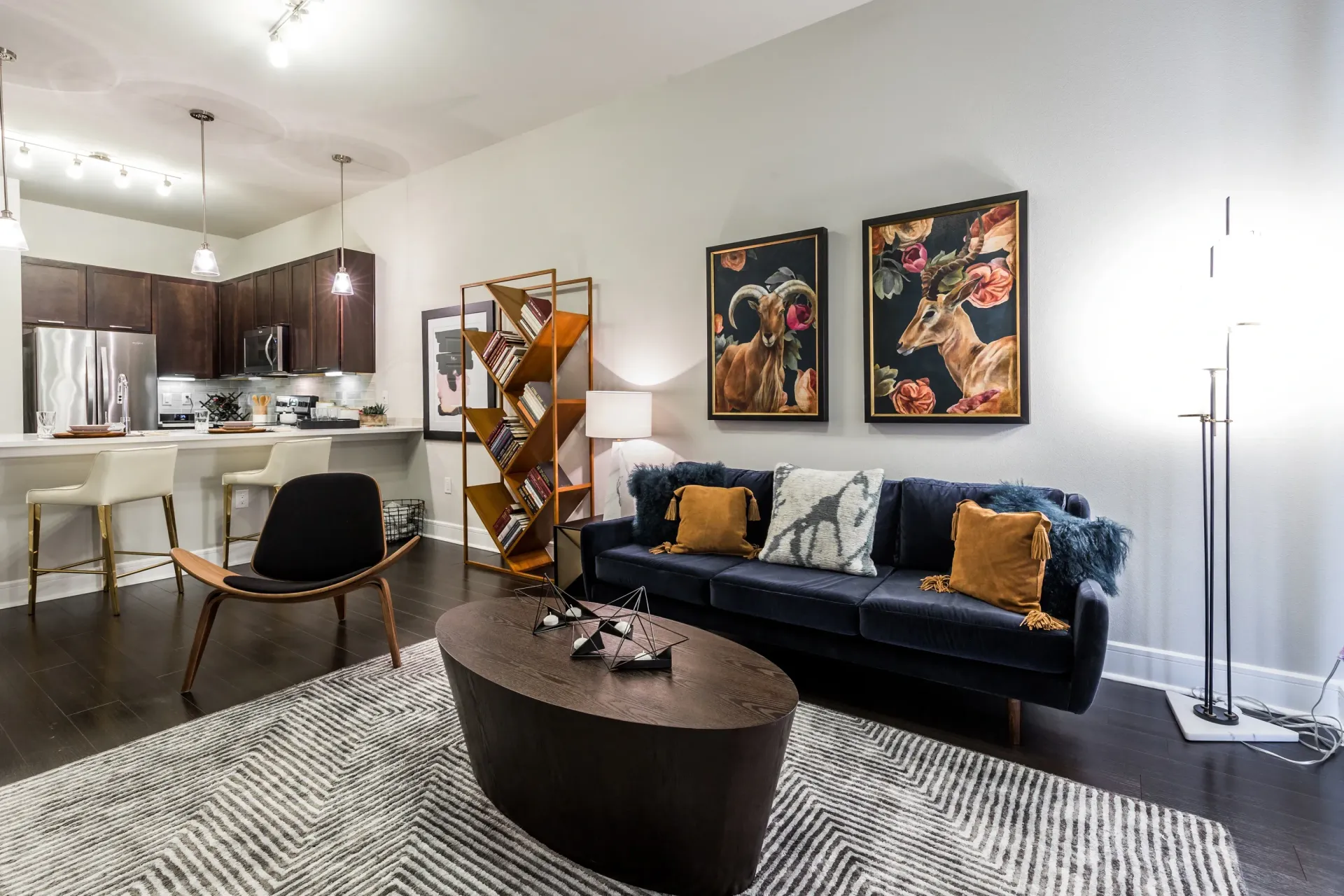 Modern living room and kitchen area with dark wood cabinets, stainless steel appliances, and elegant seating.