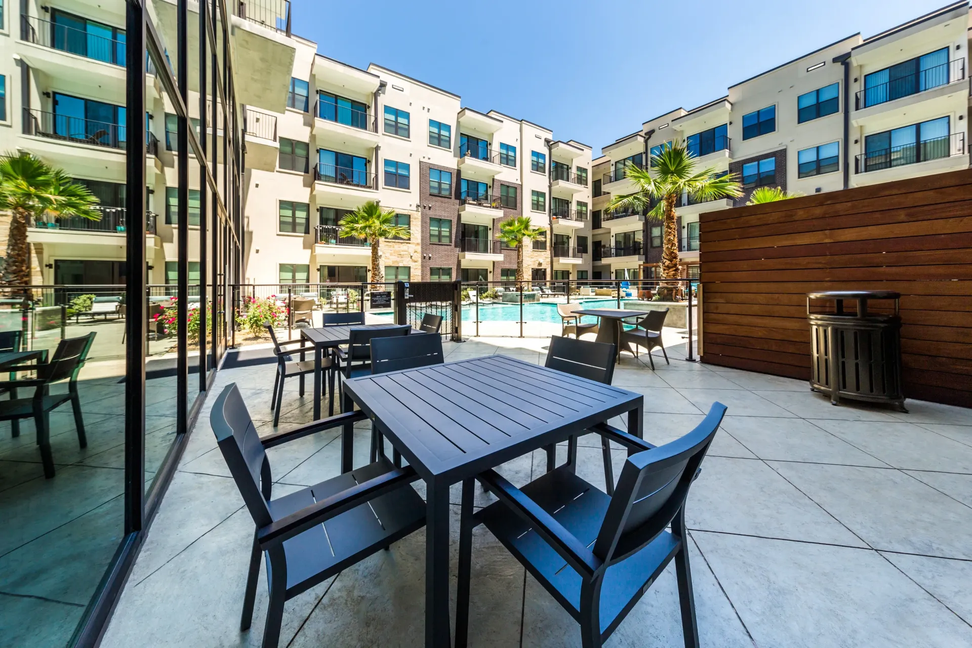Outdoor seating area with tables and chairs overlooking a swimming pool and apartment buildings.