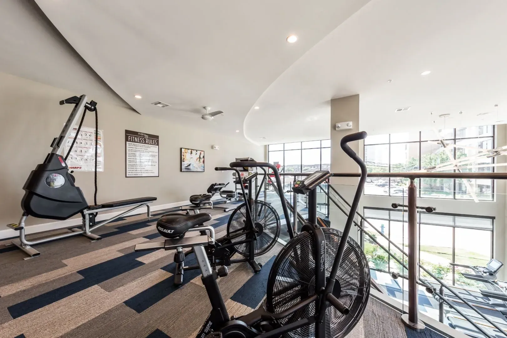A modern apartment gym with cardio equipment like air bikes, treadmills, and a rowing machine.