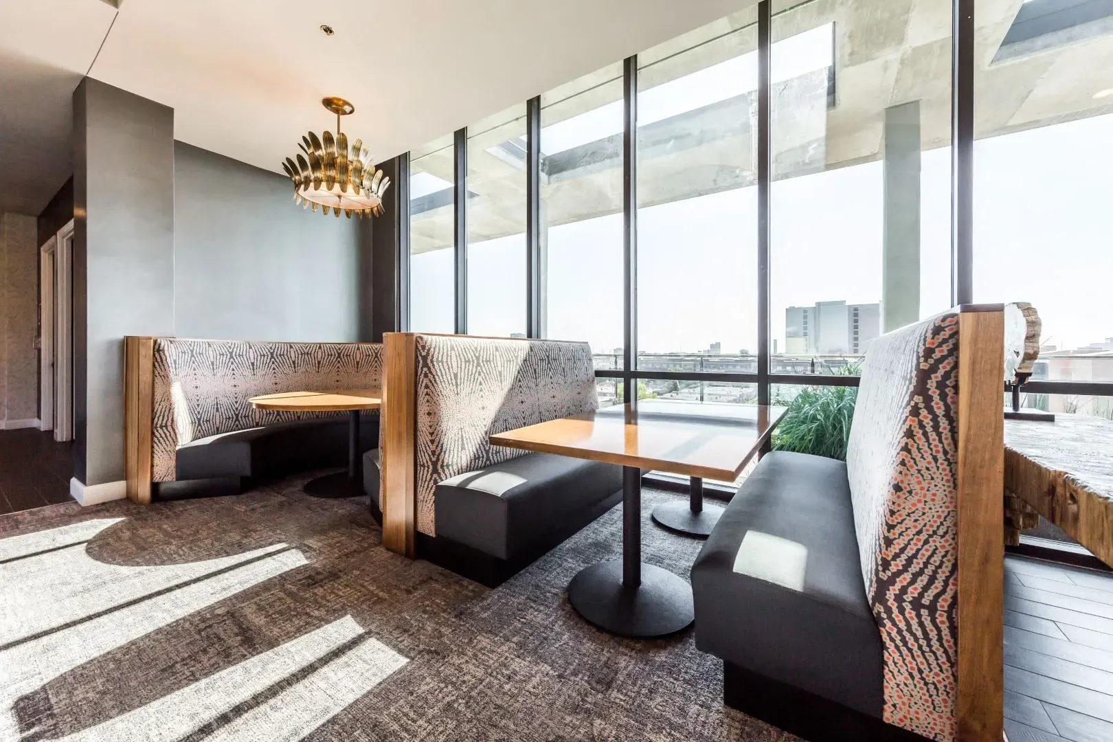 Modern dining booths with wood trim and patterned upholstery in a room with large windows and city views.