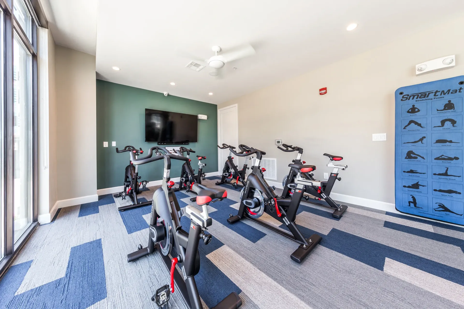 Spin bikes in a modern fitness studio with a large TV and yoga mat.