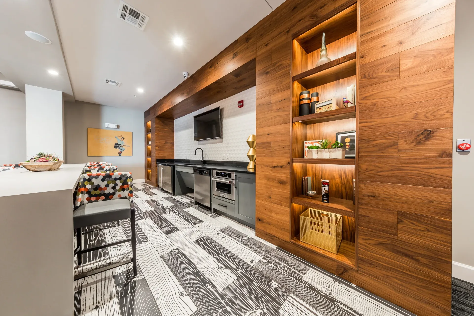 Stylish community lounge area with a wet bar, seating, and decorative shelving.